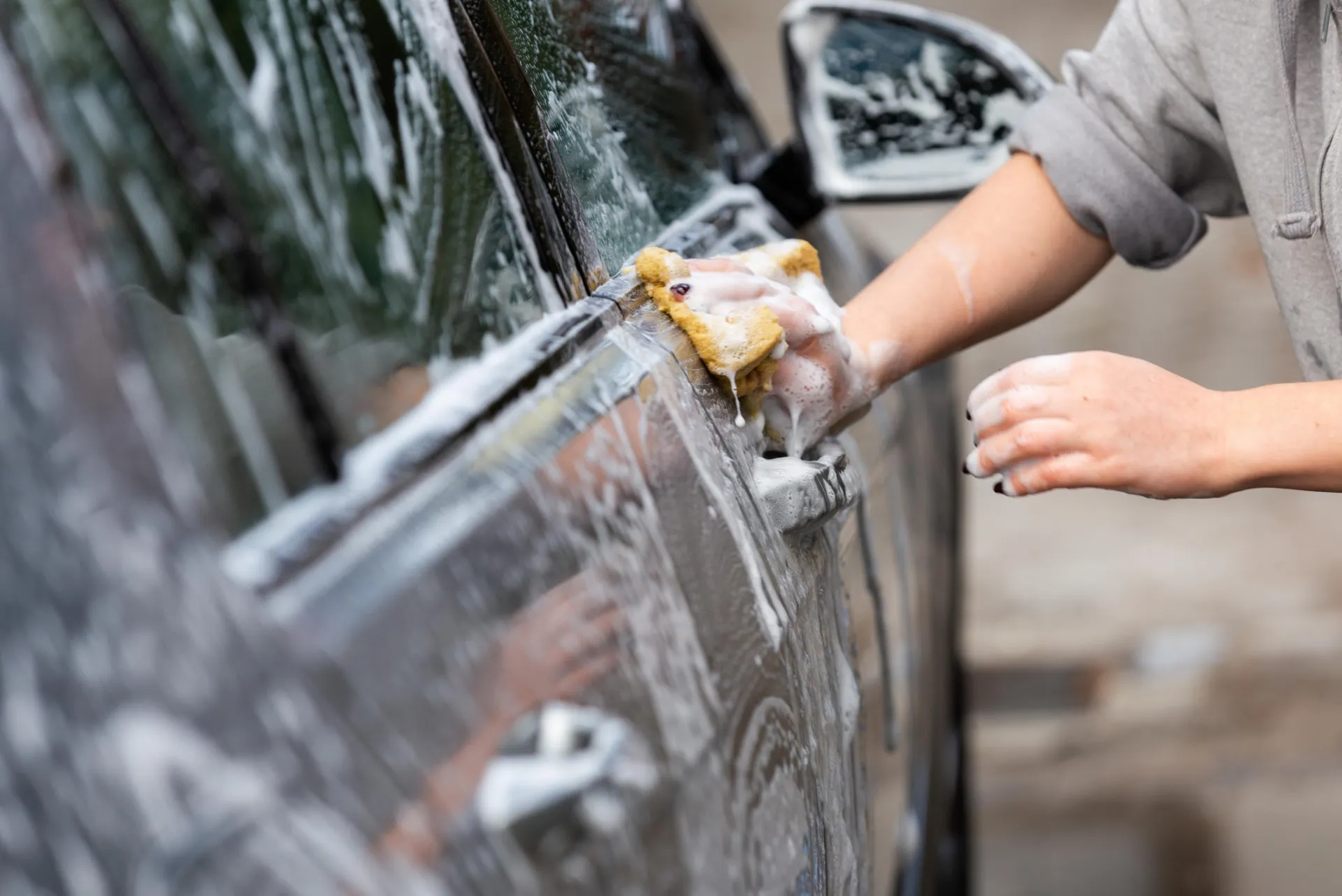 Hand washing a car door with a soapy sponge during a mobile exterior hand wash in Rhode Island